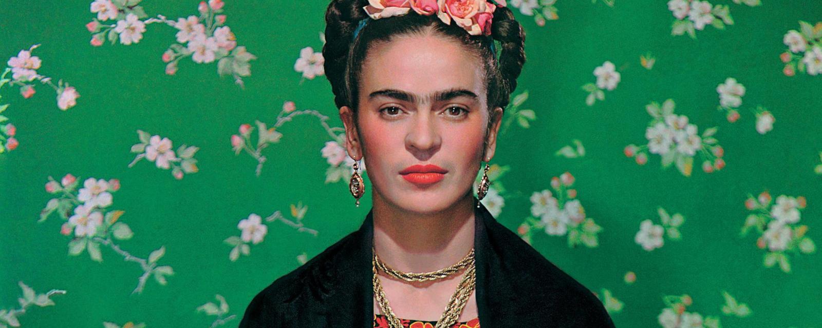 Artist Frida Kahlo seen in front of green wallpaper with floral print