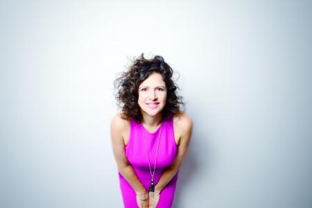 Anat Cohen wearing a bright pink dress and leaning toward the camera
