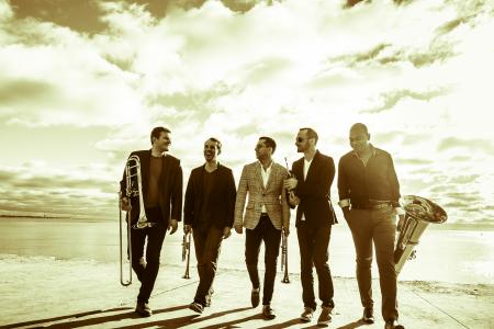 Sepia-toned photo of Axiom Brass with instruments walking outside