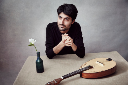 Alon Sariel sits at a table with a single flower in a black vase and a lute