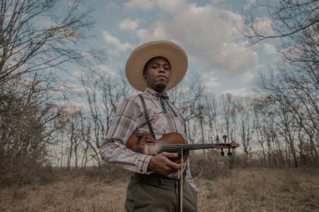 A man standing in a field, holding a fiddle.