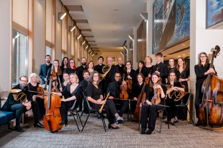 A large group of musicians, in black, posing with their instruments