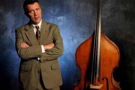 A man in a suit, standing beside an upright double bass.