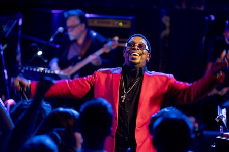 A man in a brightly colored suit with arms outstretched, performing for a large crowd.