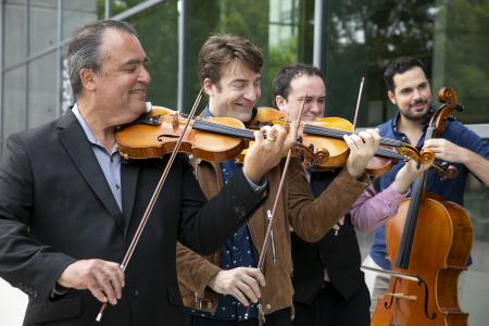 Four men standing in a line, playing stringed instruments.
