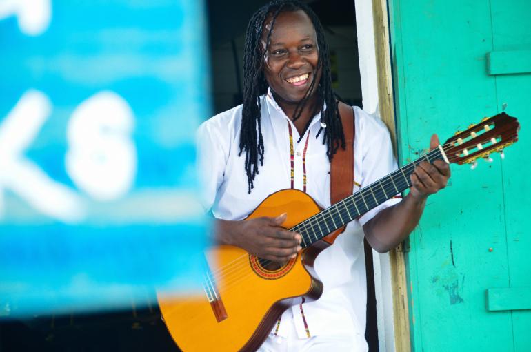 Aurelio Martinez holds a guitar next to blue and green walls