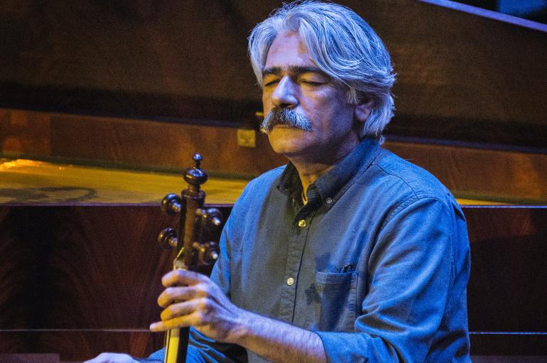 Kayhan Kalhor playing kamancheh onstage in blue light with eyes closed