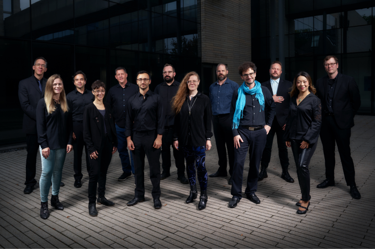 A larger group of people in black posing in front of a modern building.