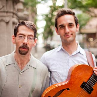 Julian Lage stands next to Fred Hersch holding a guitar