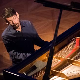 Fred Hersch, eyes closed, at an open grand piano