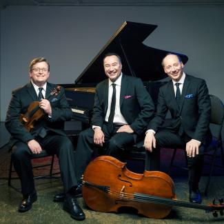 The Montrose Trio sitting in suits with instruments in front of a grand piano