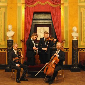 The Danish String Quartet in an opulent room dressed in suits with their instruments