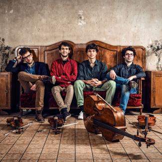 The four young men of Vision String Quartet sit on an antique sofa with their instruments in front of them
