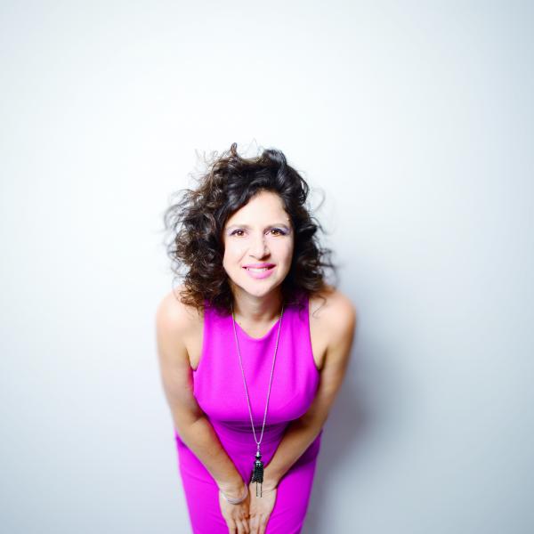 Anat Cohen wearing a bright pink dress and leaning toward the camera