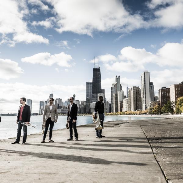 Axiom Brass standing with instruments outside, with the Chicago skyline in the background