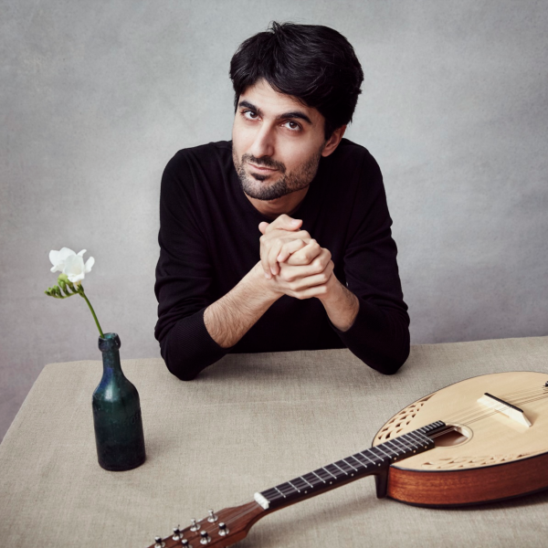 Alon Sariel sits at a table with a single flower in a black vase and a lute