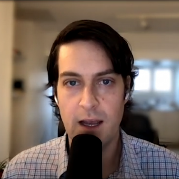 Sam Pluta speaking closely into a microphone. The room behind him appears blurry.