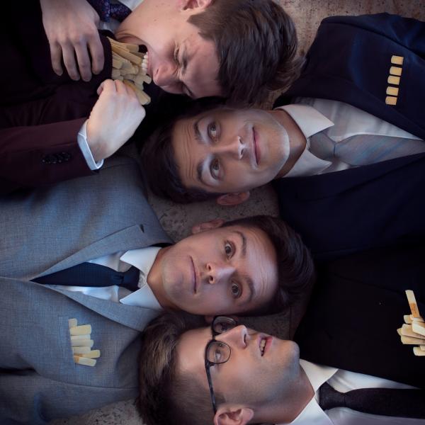 ~Nois saxophone quartet laying with their heads next to each other. The two in the middle, Brandon Quarles and Janos Csontos, face the camera. Jordan Lulloff on the bottom turns his head to the middle two, and Hunter Bockes, top, tries to bite a pocketful of saxophone reeds.