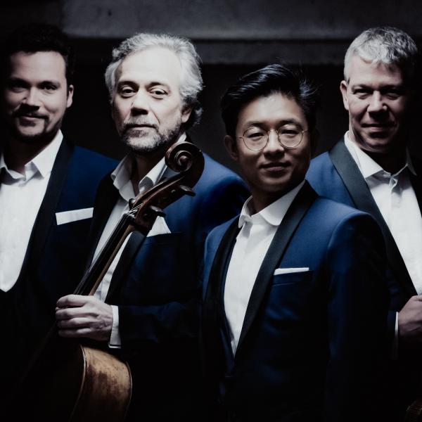 all-male string quartet posed in dark lighting with their instruments