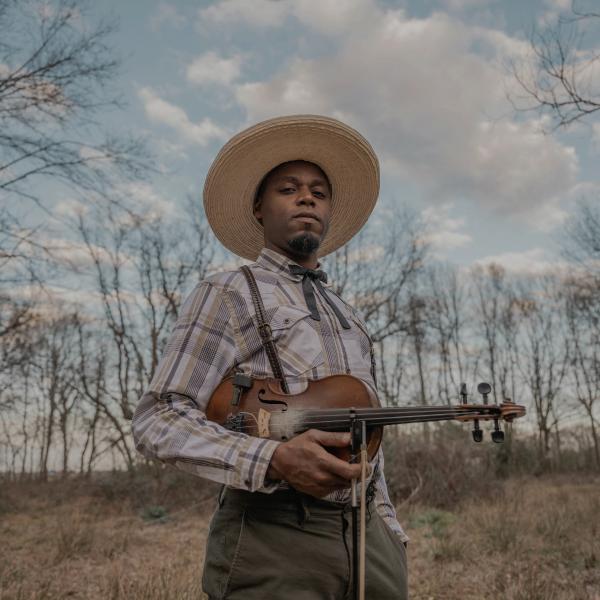 A man standing in a field, holding a fiddle.