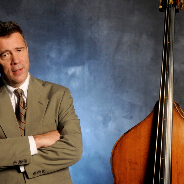 A man in a suit standing to the left on an upright double bass. 