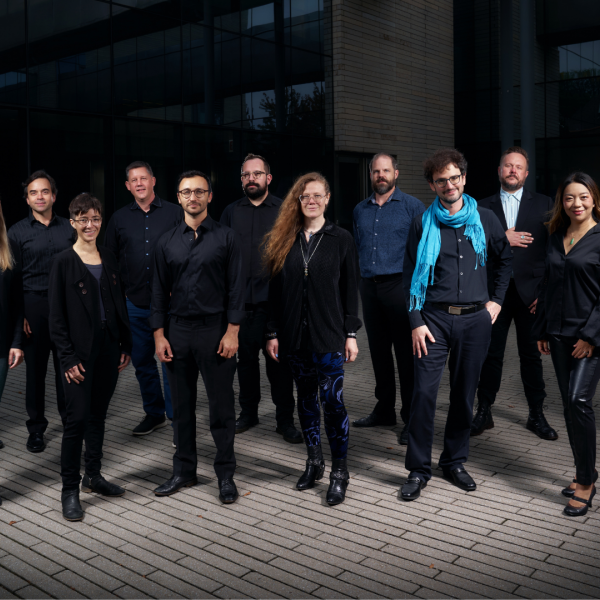 A larger group of people in black posing in front of a modern building. 