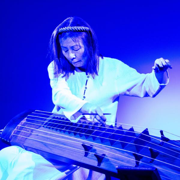Woman sits and plays a stringed instrument.