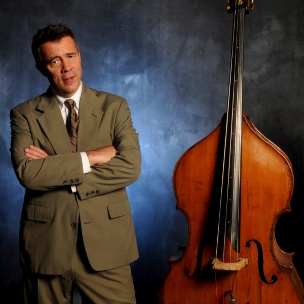 A man in a suit, standing beside an upright double bass.