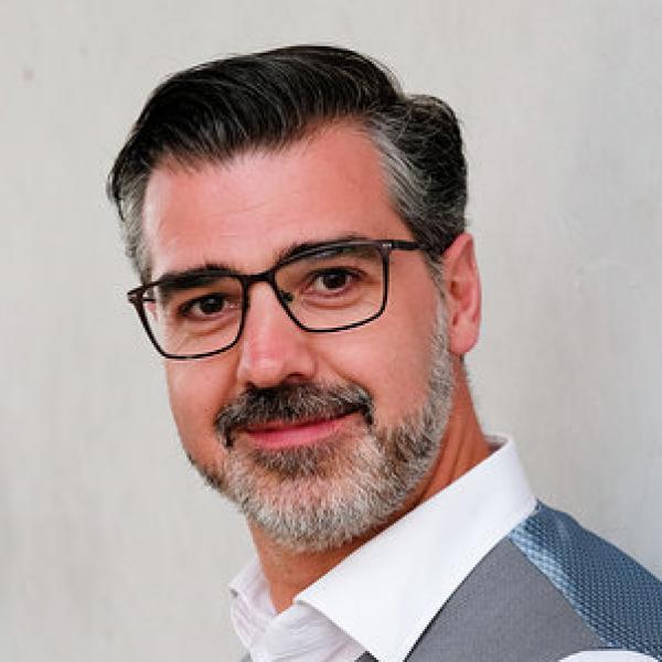 A headshot of a man in a vest. 