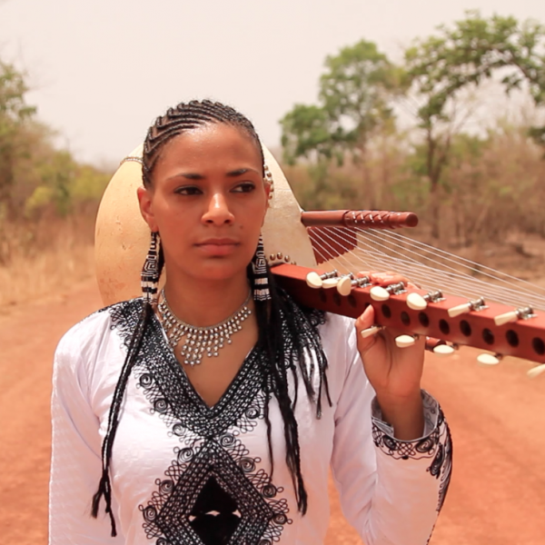 A woman walking on a path in nature with a stringed instrument over her shoulder.