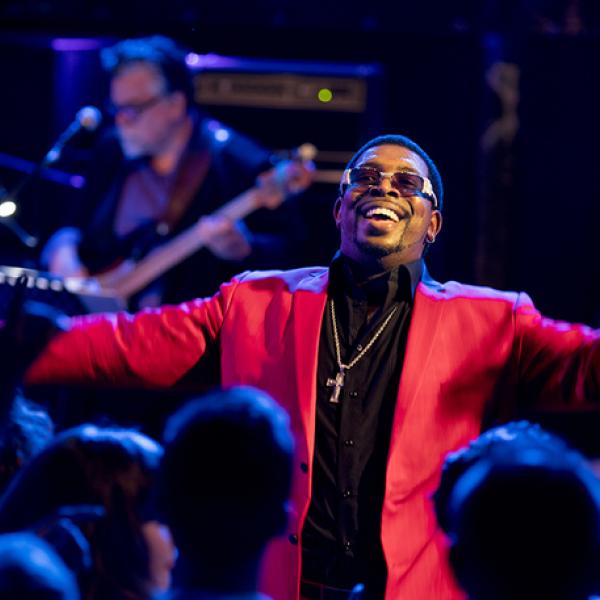 A man in a brightly colored suit with arms outstretched, performing for a large crowd.