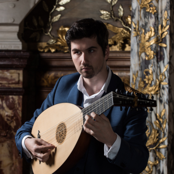 A man stands against an ornate background, playing the lute. 