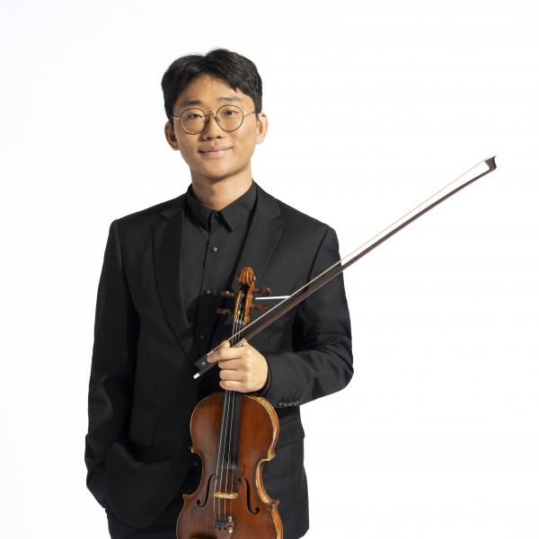 Headshot of a man in a black suit and glasses smiling while holding a violin
